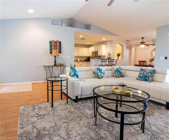 Living area with a ceiling fan, lofted ceiling, arched walkways, light wood-type flooring, and recessed lighting