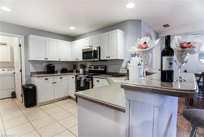 Kitchen with washer / clothes dryer, stainless steel appliances, a peninsula, white cabinets, and recessed lighting