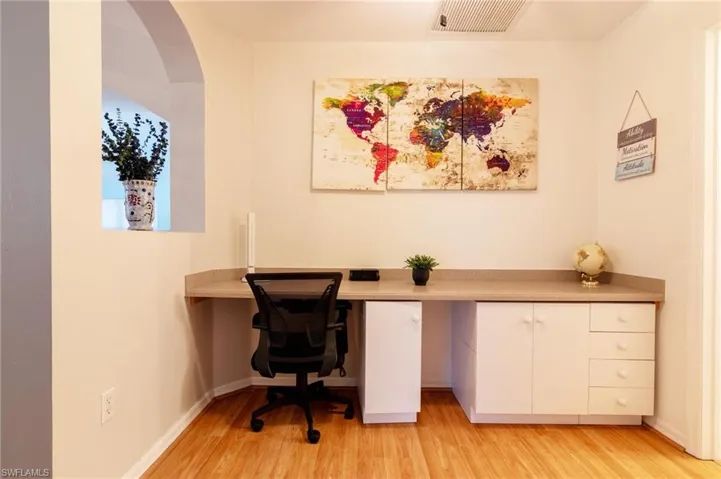 Office area featuring built in desk, light wood finished floors, arched walkways, and baseboards