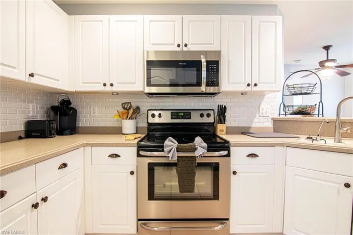 Kitchen featuring appliances with stainless steel finishes, a sink, white cabinetry, and tasteful backsplash