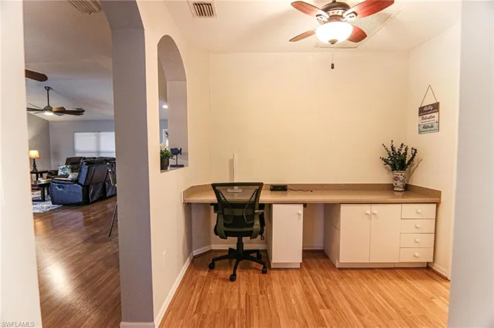 Home office with ceiling fan, light wood-type flooring, built in desk, arched walkways, and baseboards