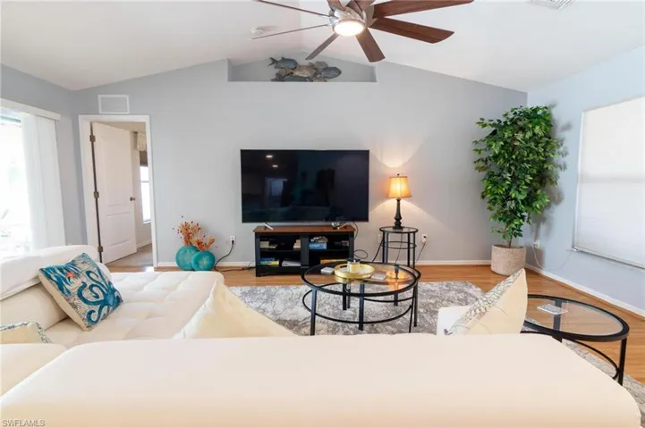Living room featuring lofted ceiling, wood finished floors, ceiling fan, and baseboards