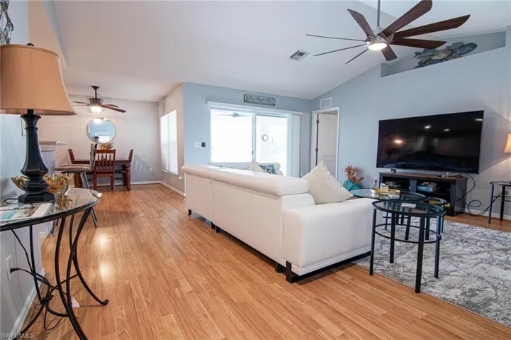 Living room featuring ceiling fan, light wood finished floors, lofted ceiling, and baseboards