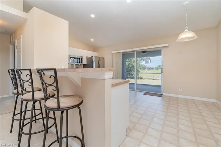 Kitchen with stainless steel appliances, a breakfast bar area, white cabinetry, light countertops, and decorative light fixtures