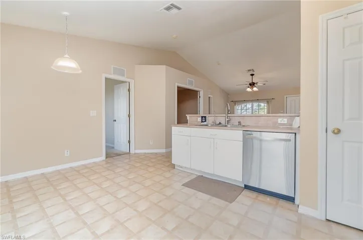 Kitchen with pantry and stainless steel dishwasher, a sink, a ceiling fan, lofted ceiling, and white cabinetry