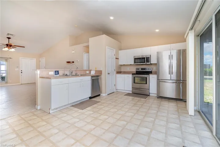 Kitchen with appliances with stainless steel finishes, lofted ceiling, a peninsula, a sink, and white cabinets