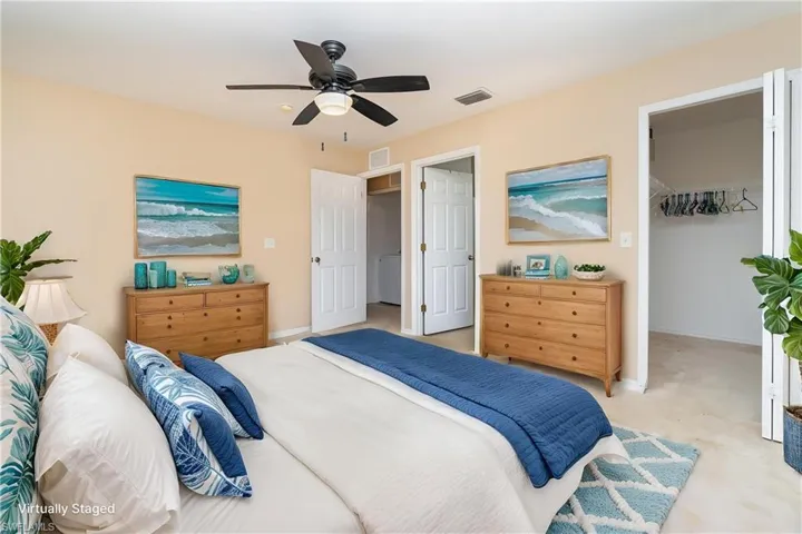 Bedroom featuring a walk in closet, baseboards, light carpet, and ceiling fan