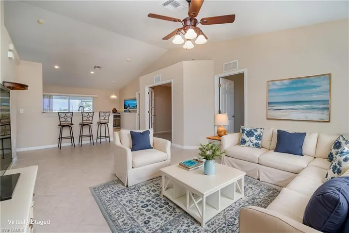 Living area with a ceiling fan, vaulted ceiling, baseboards, and light tile patterned flooring