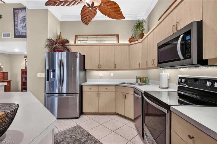 Kitchen with appliances with stainless steel finishes, light brown cabinets, crown molding, light countertops, and light tile patterned flooring