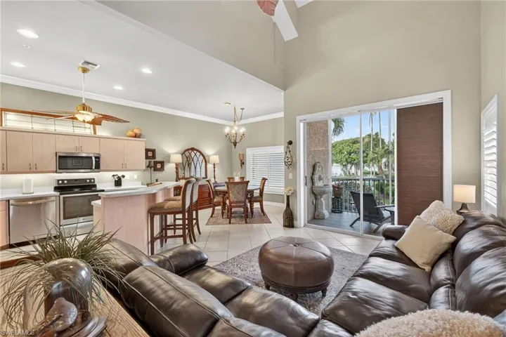 Living area featuring ceiling fan, light tile patterned floors, ornamental molding, a chandelier, and a high ceiling