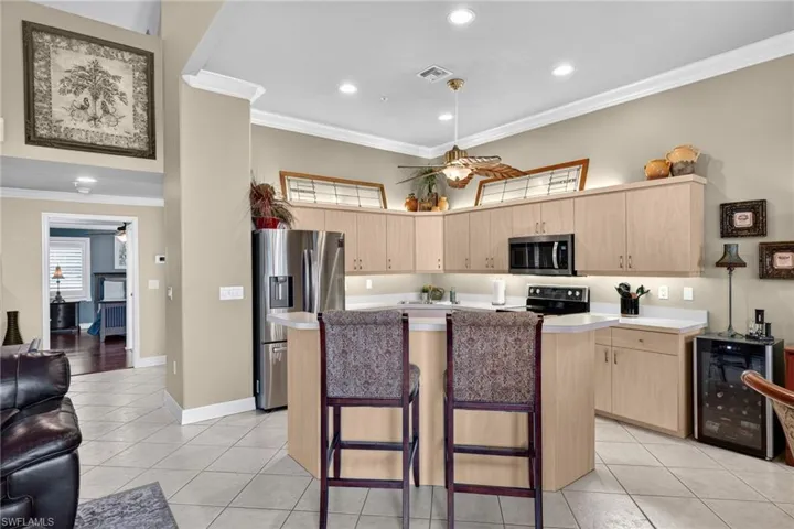 Kitchen featuring a ceiling fan, a kitchen breakfast bar, crown molding, light brown cabinetry, and a kitchen island