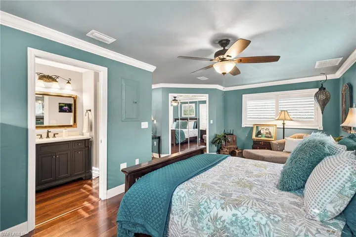 Bedroom with ornamental molding, dark wood-style flooring, a ceiling fan, ensuite bath, and electric panel