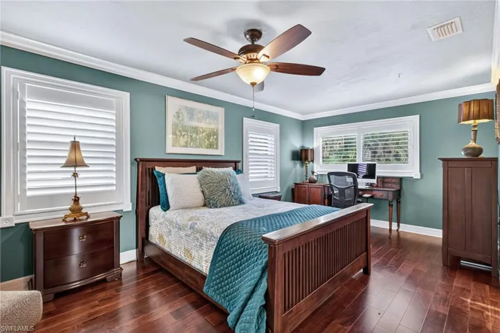Bedroom featuring dark wood finished floors, ornamental molding, a ceiling fan, and an office area