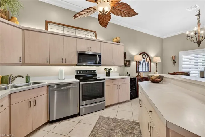 Kitchen featuring light brown cabinets, appliances with stainless steel finishes, ornamental molding, light countertops, and light tile patterned flooring