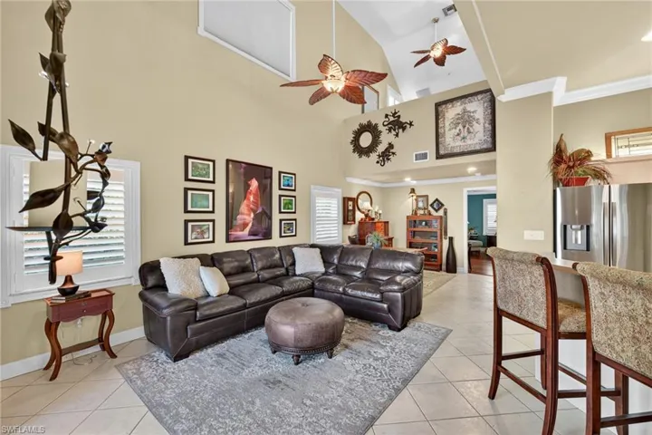 Living area with a ceiling fan, light tile patterned flooring, high vaulted ceiling, and ornamental molding