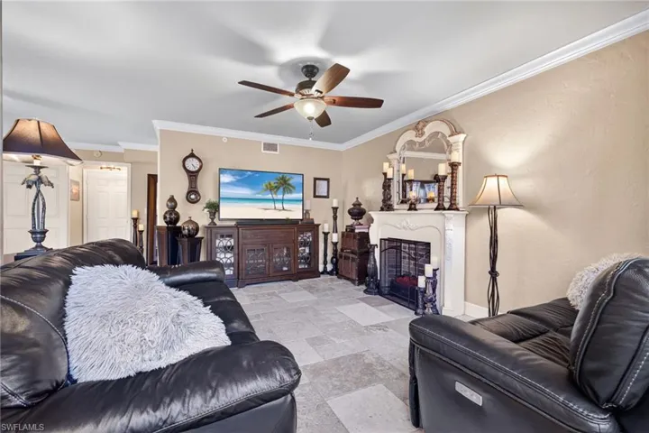 Living area featuring ornamental molding, a fireplace with flush hearth, stone tile flooring, and a ceiling fan