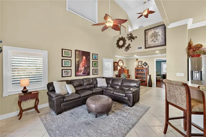 Living room featuring a ceiling fan, light tile patterned floors, high vaulted ceiling, ornamental molding, and healthy amount of natural light