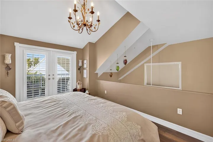 Bedroom featuring access to outside, dark wood-type flooring, french doors, vaulted ceiling, and a chandelier Loft