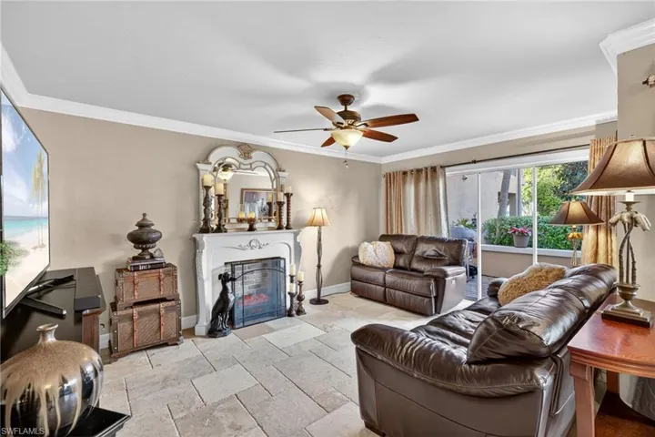 Family room with crown molding, a glass covered fireplace, ceiling fan, and stone tile flooring