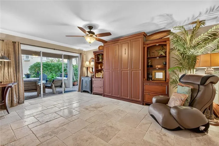 Living area featuring crown molding, a ceiling fan, and stone tile flooring Murphy bed