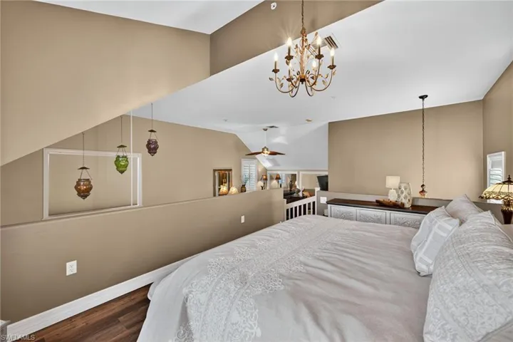 Bedroom featuring wood finished floors, vaulted ceiling, and a chandelier Loft