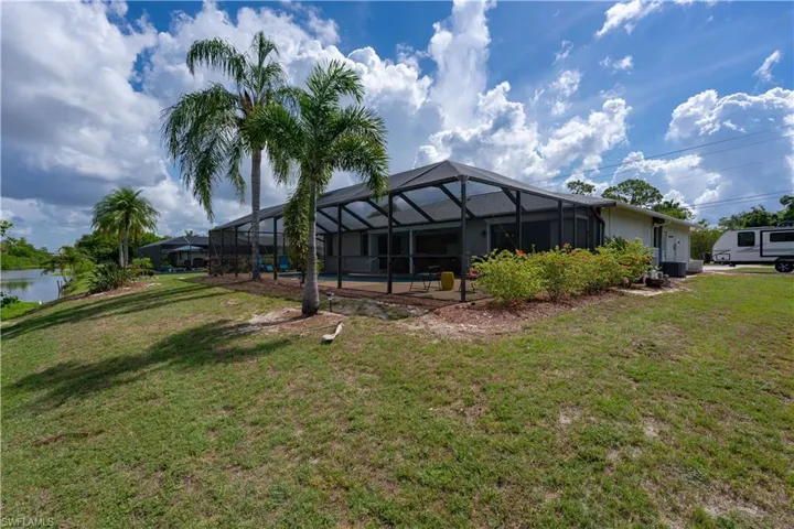 Rear view of house featuring a lawn, an outdoor pool, and a lanai