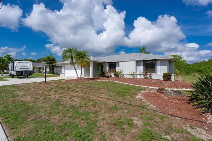 Ranch-style house featuring a garage, driveway, stucco siding, and a front lawn
