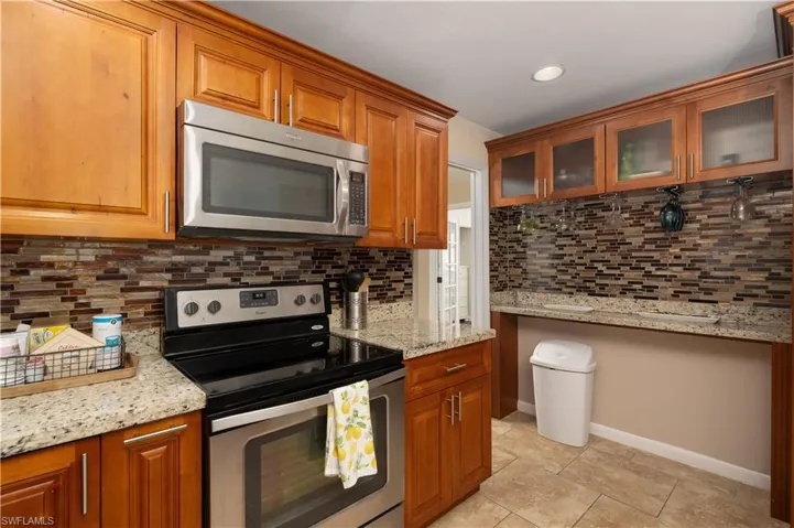 Kitchen with stainless steel appliances, tasteful backsplash, brown cabinets, light stone counters, and light tile patterned floors