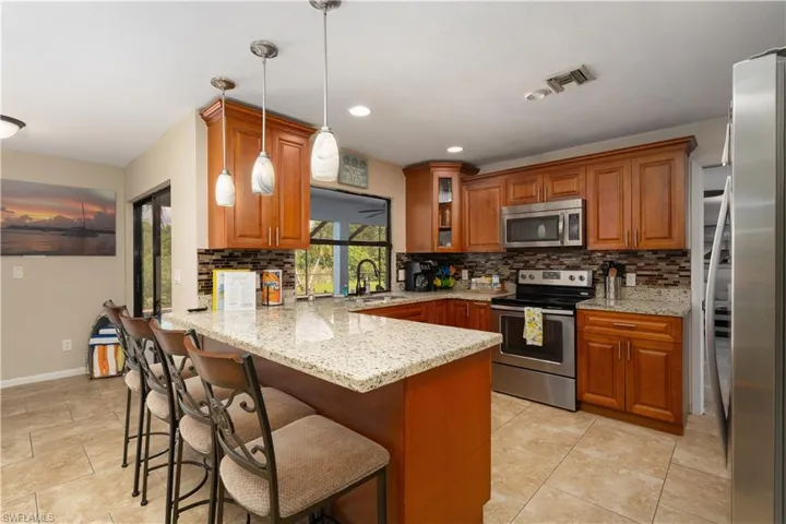 Kitchen with stainless steel appliances, a peninsula, a sink, brown cabinets, and recessed lighting