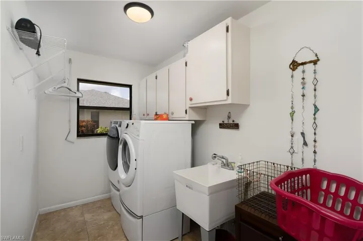 Washroom featuring washer and clothes dryer, cabinet space, baseboards, and light tile patterned flooring