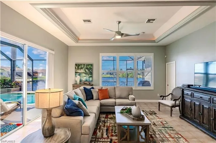 Living room with ceiling fan, light tile patterned floors, a tray ceiling, and healthy amount of natural light