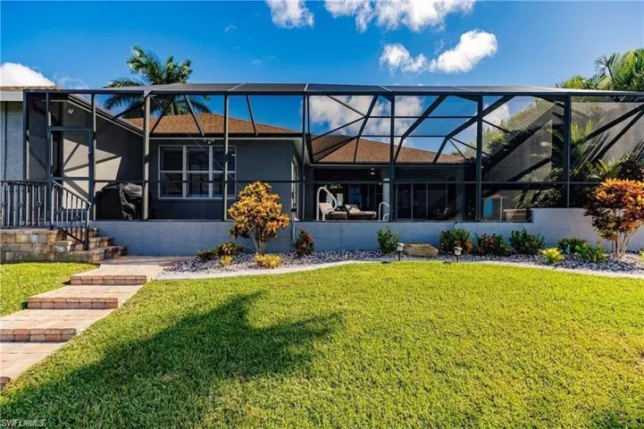 Rear view of house with a lanai, a sunroom, a lawn, and stucco siding
