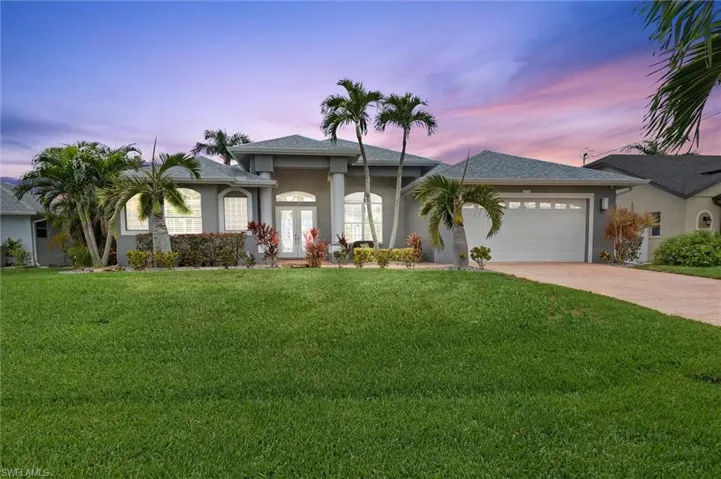 View of front of home with a lawn, stucco siding, an attached garage, concrete driveway, and french doors