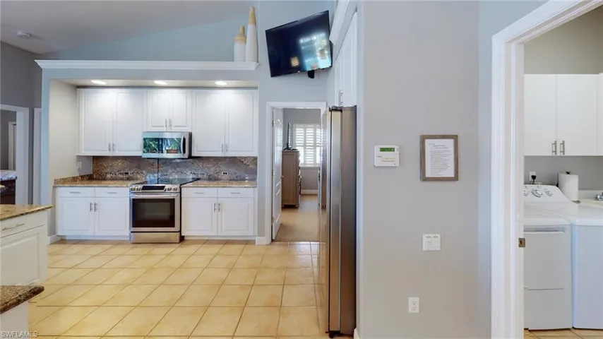 Kitchen with white cabinets, appliances with stainless steel finishes, lofted ceiling, light tile patterned floors, and washing machine and dryer