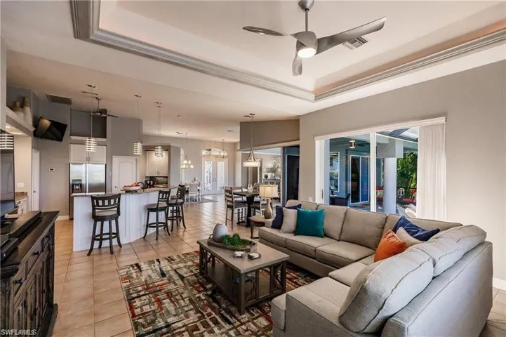 Living room featuring a ceiling fan, light tile patterned floors, plenty of natural light, a tray ceiling, and crown molding
