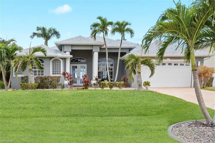 View of front facade with french doors, stucco siding, driveway, a front lawn, and a garage