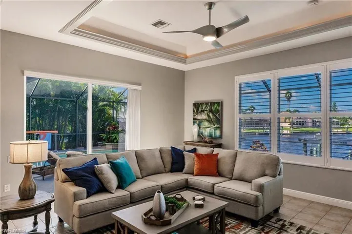 Tiled living area featuring a tray ceiling, a ceiling fan, a water view, and a sunroom