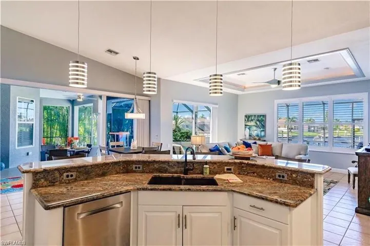 Kitchen with light tile patterned floors, open floor plan, white cabinets, hanging light fixtures, and lofted ceiling