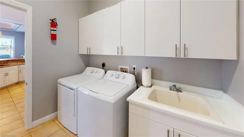 Laundry room featuring light tile patterned floors, washing machine and dryer, and cabinet space access to garage