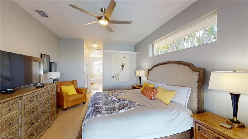 Carpeted bedroom with multiple windows, ceiling fan, and ensuite bath