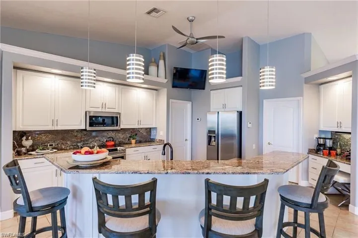 Kitchen featuring light tile patterned flooring, a breakfast bar, light stone counters, decorative backsplash, and appliances with stainless steel finishes