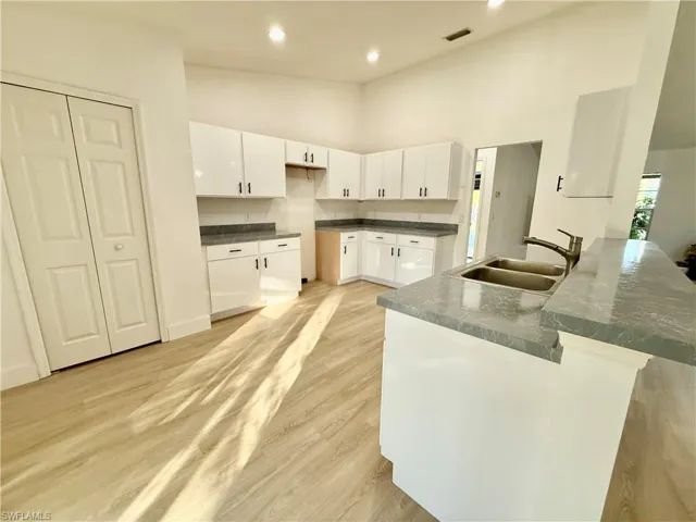Kitchen featuring a sink, white cabinetry, a peninsula, light wood-style flooring, and a high ceiling
