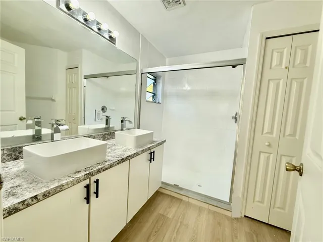 Bathroom featuring a closet, double vanity, a stall shower, and wood finished floors