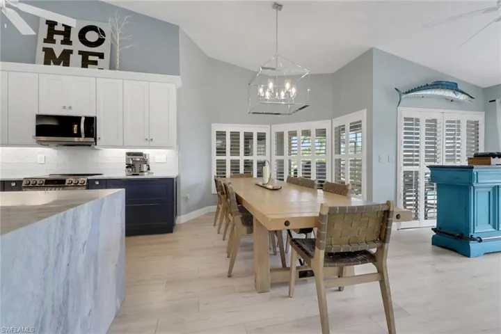 Dining room with a ceiling fan, high vaulted ceiling, light wood-style floors, and a chandelier