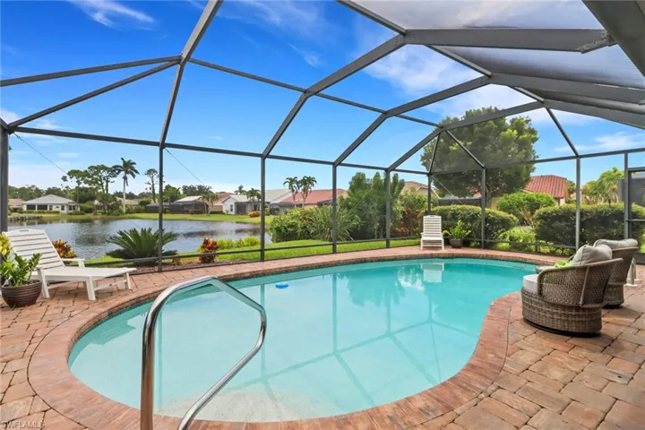 Swimming pool with glass enclosure, a sunroom, a water view, and a patio area