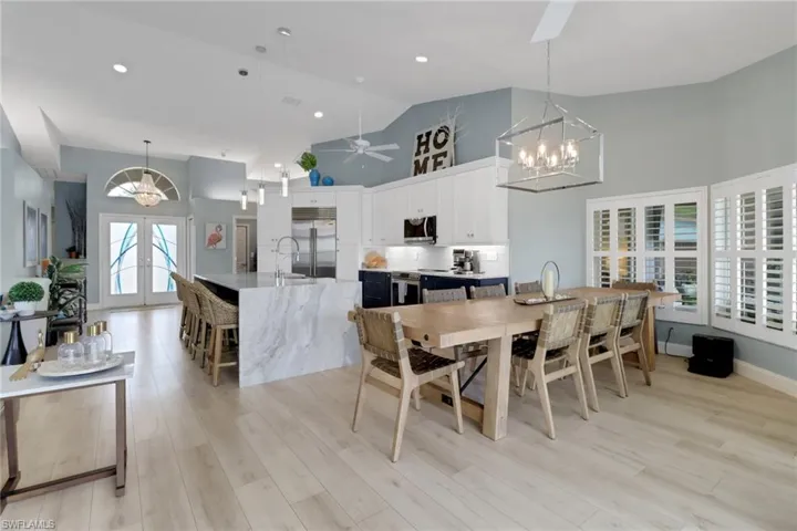 Dining space with a chandelier, ceiling fan, french doors, light wood finished floors, and high vaulted ceiling