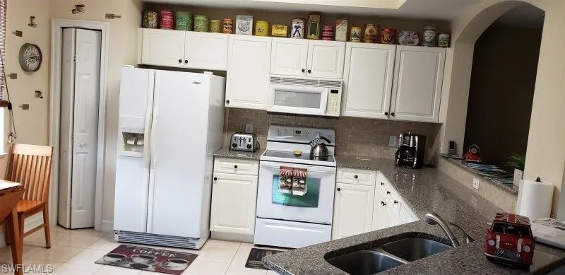 Kitchen featuring white appliances, white cabinets, dark stone countertops, decorative backsplash, and light tile patterned floors