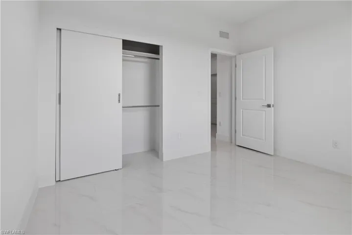 Bright interior space featuring large format tile flooring, white walls, and a sliding closet door with built-in shelving