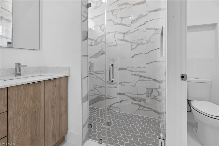 Glass-enclosed shower with white marble-look subway tile surround and gray hexagonal tile flooring