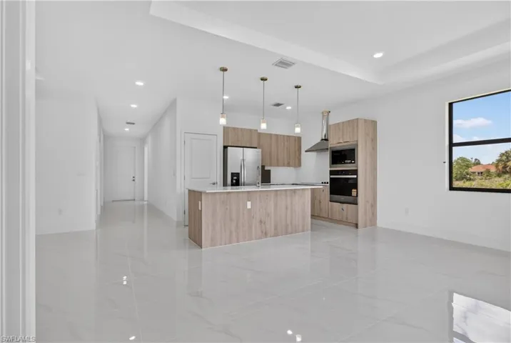 Open-concept kitchen featuring wood-finish cabinetry, a central island with countertop seating, stainless steel appliances, and contemporary pendant lighting